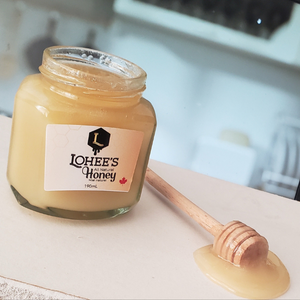 190 ml of lohees natural honey on a kitchen counter with a honey dipper dripping honey